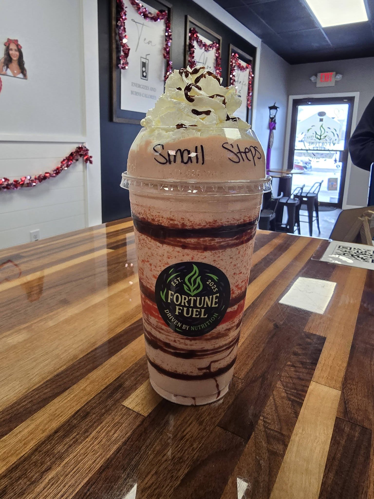 A layered protein shake topped with whipped cream and chocolate drizzle, marked &lsquo;Small Steps&rsquo;, on a Fortune Fuel table in Somers